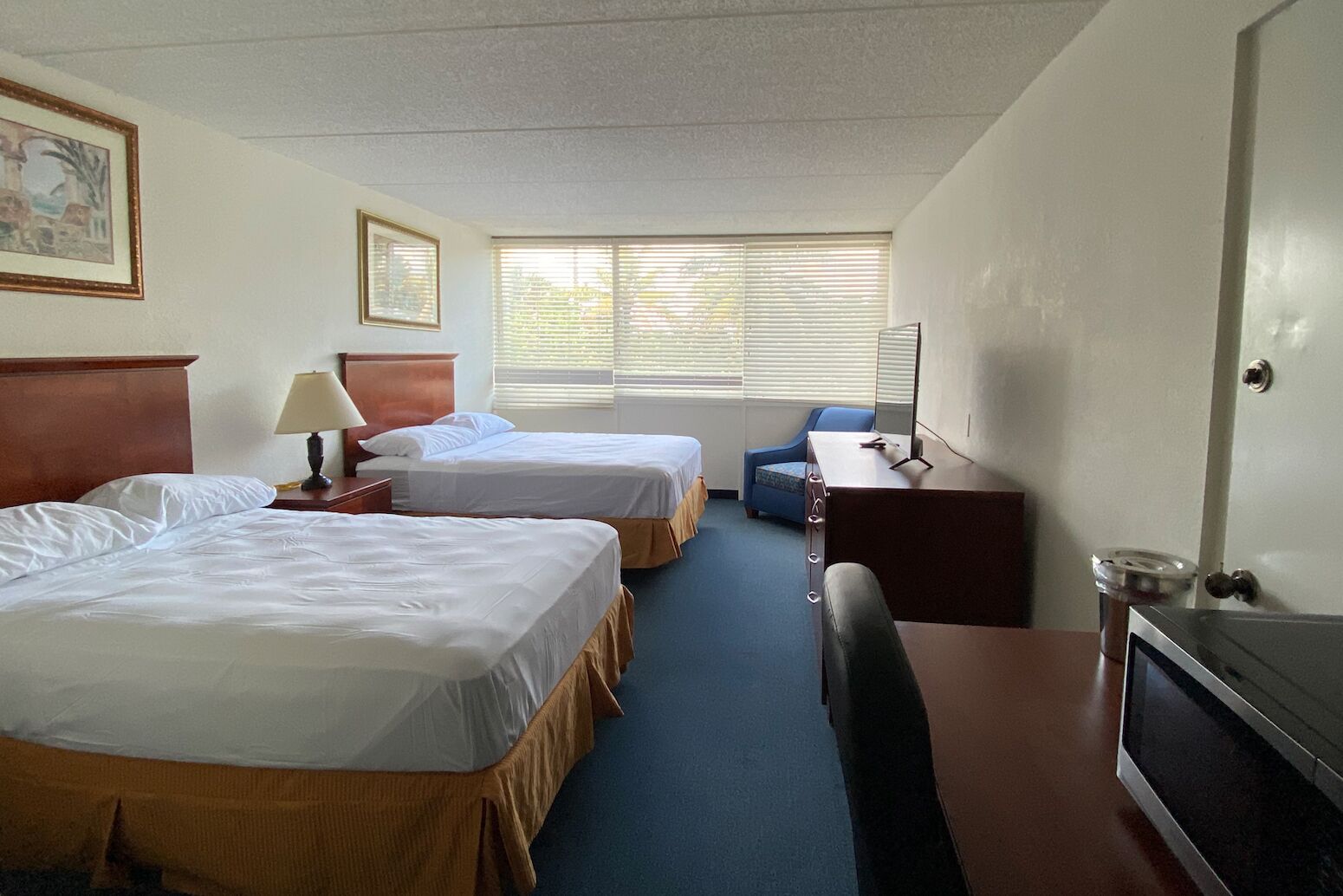 A hotel room with two beds, a desk, a chair, a TV, and a window with blinds.