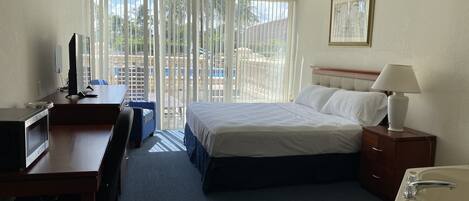 A hotel room with a bed, desk, computer, and a view of the outdoors through large windows.