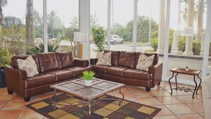 Ein Wohnzimmer mit einem braunen Ledersofa, einem Couchtisch aus Holz mit einer Pflanze und einem gemusterten Teppich.