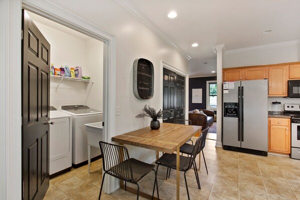 A modern kitchen with a wooden dining table, chairs, a refrigerator, and a microwave.