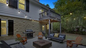 Een terras met tuinmeubilair, een barbecue en lichtjes.