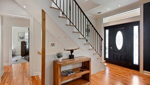 Een modern interieur met een houten trap, een zwarte deur met een ruit en een houten consoles met een tijdschrift.