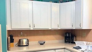 A kitchen with white cabinets, a coffee maker, and a kettle on the countertop.