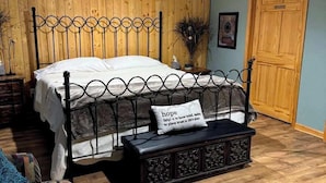 A bedroom with a wooden paneled headboard, a bed with white linens, a black metal bench with a pillow, and a wooden door labeled "PRIVATE".