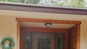 A brick house with a brown front door, a wreath on the wall, and two potted plants on the porch.
