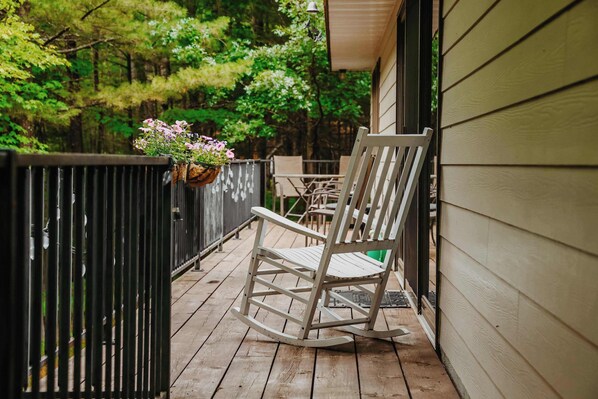 A rocking chair on a wooden deck with a hanging flower basket.
