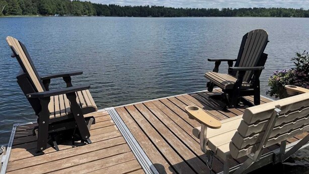 A wooden dock with two Adirondack chairs facing a calm lake and a forested shoreline.