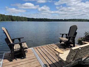 A wooden dock with two Adirondack chairs facing a calm lake and a forested shoreline. - Brandy Bay Hideaway: PET FRIENDLY (Woodruff)