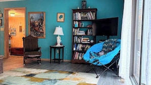 A living room with a teal wall, a bookshelf, a television, a blue chair, and a patterned rug.