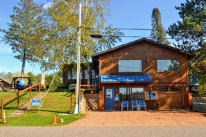 En träbyggnad med ett blått markis, en ytterdörr och en liten veranda med stolar.