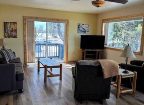 A living room with a sofa, a table, a TV, and a lamp. There is a sliding glass door leading to a balcony.