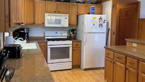 A kitchen with wooden cabinets, a microwave, a refrigerator, and a stove. - Camp Pinemere - Private Northwoods Retreat (Minocqua)