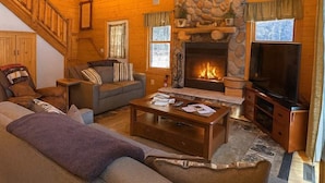 A cozy log cabin interior with a fireplace, a sofa, a television, and a staircase. - Camp Pinemere - Private Northwoods Retreat (Minocqua)
