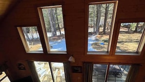 A cabin with multiple skylights, a dining area, and a view of a forested area. - Camp Pinemere - Private Northwoods Retreat (Minocqua)