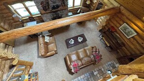 A log cabin interior with a stone fireplace, wooden beams, and a cozy seating area with leather sofas. - Katherine Lake Lodge (Hazelhurst)