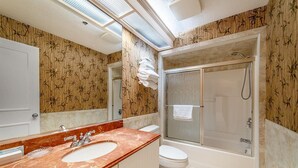 Een badkamer met een marmeren wastafel, toilet, douche met glazen wanden en muren met bamboetextuur.