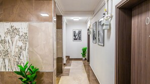 A hallway with a marble floor, a potted plant, framed pictures on the walls, and a door at the end. - Intercity Residence - Private apartments (Cluj-Napoca)