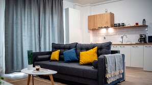 A modern living room with a grey sofa, yellow and blue cushions, a coffee table, and a kitchen area with wooden cabinets and a coffee machine. - Intercity Residence - Private apartments (Cluj-Napoca)