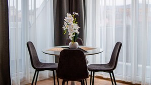 A dining area with a round table, two chairs, a vase with flowers, and a view through sheer curtains. - Intercity Residence - Private apartments (Cluj-Napoca)
