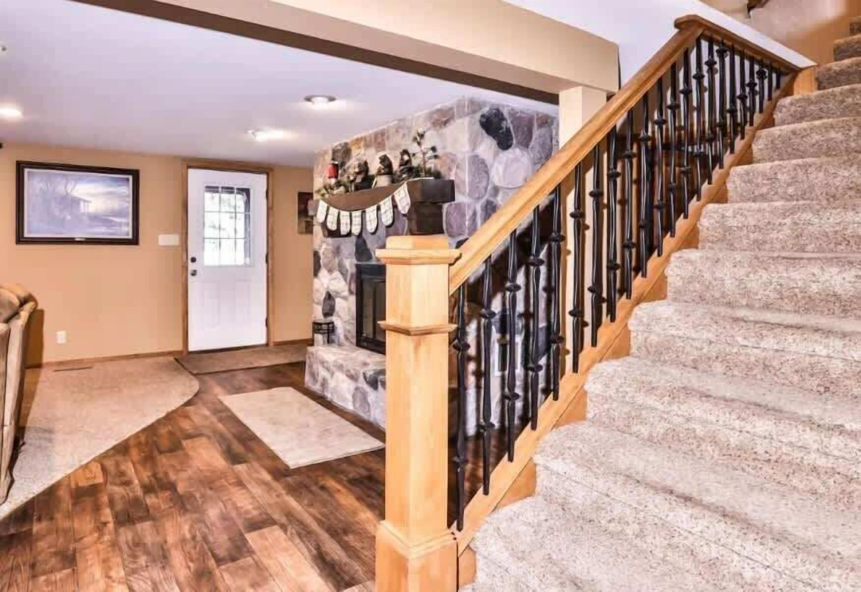 Un escalier avec une rampe en bois et des marches en pierre, menant à une pièce dotée d’un mur en pierre et d’une porte.