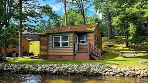 Een chalet met een veranda, een kleine trap en een picknicktafel in een bebost gebied.