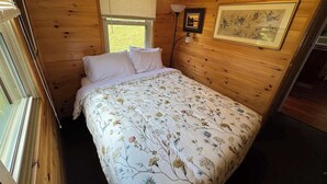 Een houten kamer met een bed, een raam en een wandlamp.