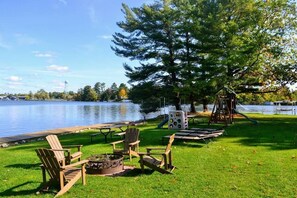 Un parc au bord du lac, équipé de chaises en bois, d’un foyer, de tables de pique-nique et d ’une aire de jeux.
