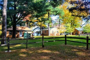 A rustic cabin with a boat trailer parking area, surrounded by trees and a wooden fence.
