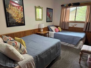 Une chambre avec deux lits, une petite table et une fenêtre avec des rideaux.