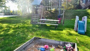 Un parc infantil amb tobogan, cadira de balanceig i taula de pícnic.