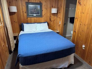 A room with a bed, wooden walls, and two wall-mounted lamps.