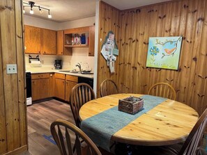 Une pièce aux murs lambrés, comprenant une table à manger, des chaises, un coin cuisine et un tableau accroché au mur.
