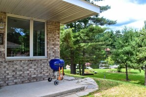 A brick house with a covered porch, a barbecue grill, and a well-maintained lawn with trees.