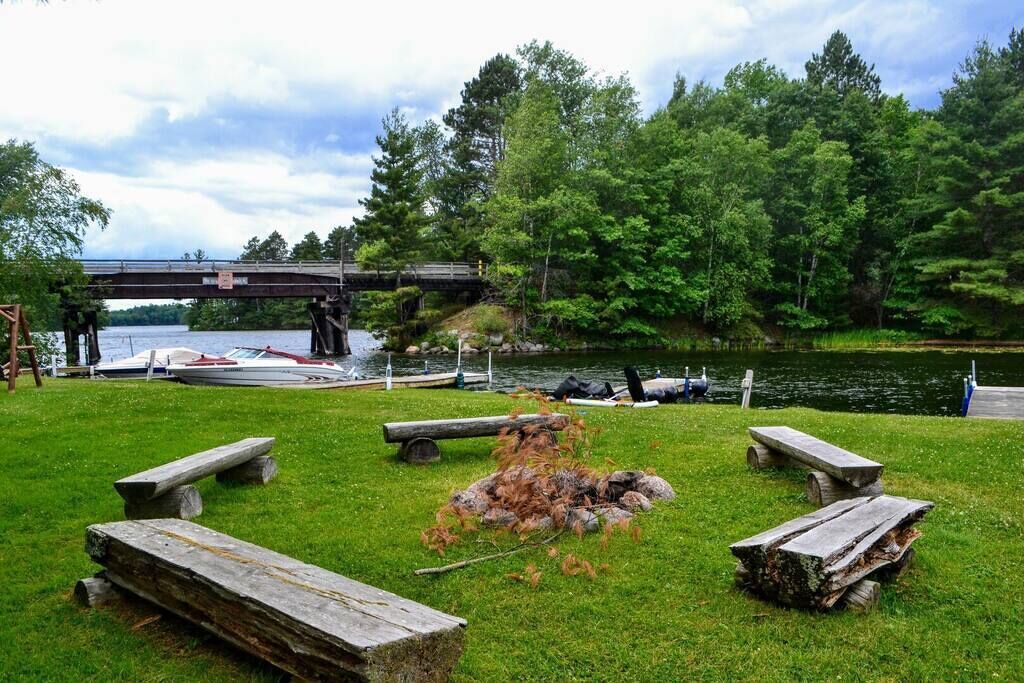 Un parque junto al lago con mesas de picnic, un pequeño puente y barcos amarrados cerca del agua.