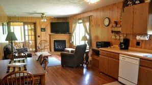 A wooden interior with a dining area, a fireplace, a television, and a kitchen with a dishwasher.