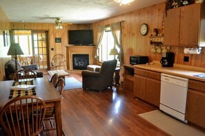 A wooden interior with a dining area, a fireplace, a television, and a kitchen with a dishwasher. - Nitschke's Resort Cabin #15 (Minocqua)