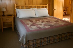 Una cama con una colcha escocesa y dos almohadas, una mesita de noche con una lámpara y un cabecero de madera.