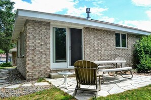 Une maison en briques dotée d’un patio comprenant une table et des chaises, une cheminée et une grande porte-fenêtre coulissante.