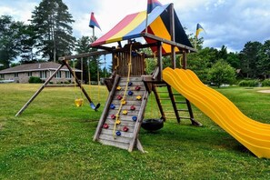 Een speeltuin met een houten klimmuur, een gele glijbaan en een schommel.