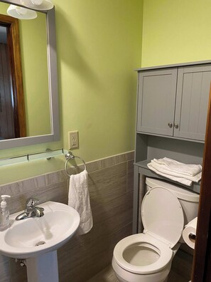 A bathroom with a white sink, a mirror, a towel rack, a toilet, and a shelf with towels.