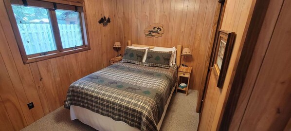 A bedroom with a plaid bedspread, two bedside lamps, a window, and a wooden wall.