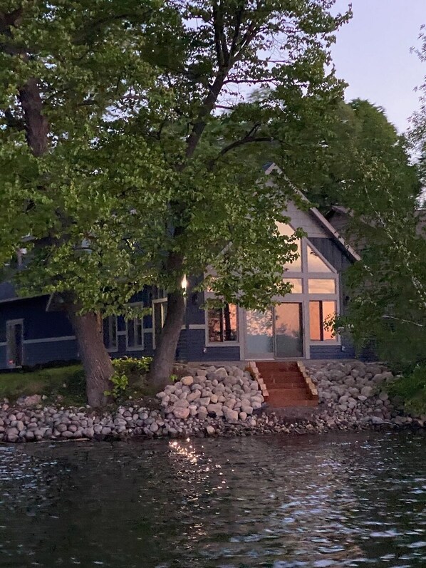 Een vakantiehuis aan het meer, met een pad van stenen dat naar de ingang leidt, omringd door bomen.