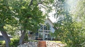 A wooden dock leading to a house with a stone wall and a boat docked on the left. - Exquisite Cottage on Lake Brophy. Lic1971 (Alexandria)