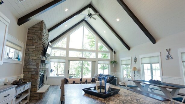 A spacious kitchen with a stone fireplace, large windows, and a high ceiling with exposed beams. - Exquisite Cottage on Lake Brophy. Lic1971 (Alexandria)
