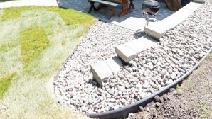 A modern house with large windows, a patio with a table and chairs, and a stone pathway. - Exquisite Cottage on Lake Brophy. Lic1971 (Alexandria)