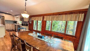 A kitchen with wooden cabinets, a dining table with chairs, and large windows with a view of trees.
