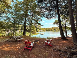 Ein Campingplatz am Seeufer mit zwei roten Adirondack-Stühlen, einem Picknicktisch und einem kleinen Steg.