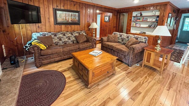 A living room with wooden walls, two sofas, a coffee table, a TV, and a ceiling fan.
