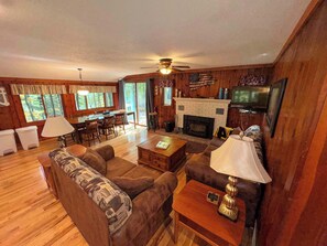 Ein gemütliches Blockhaushaus-Interieur mit Kamin, Holzwänden, einem Essbereich und einem Wohnzimmer mit Sofas und Couchtisch.