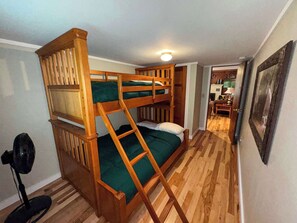 Habitación con literas, una escalera, suelo de madera y una puerta que da a una zona de cocina.